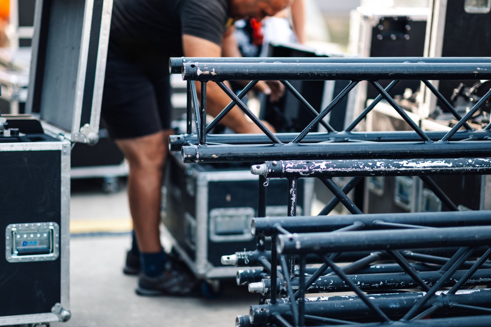 Stagehand unloads a metal truss from a road case for an outdoor concert setup, ensuring a seamless production with meticulous attention to detail and professionalism